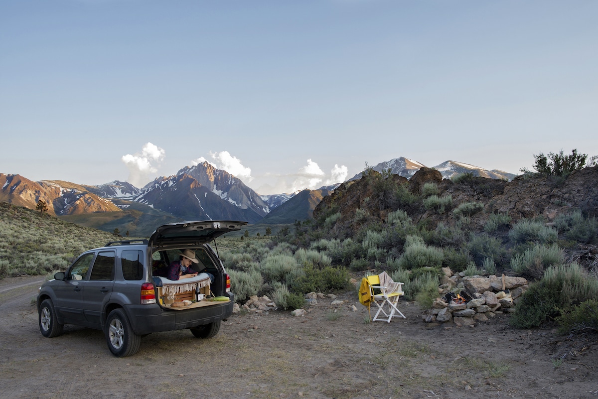 A woman lounging in the back on an SUV and looking at a cellphone with Mount Morrison in the distance.