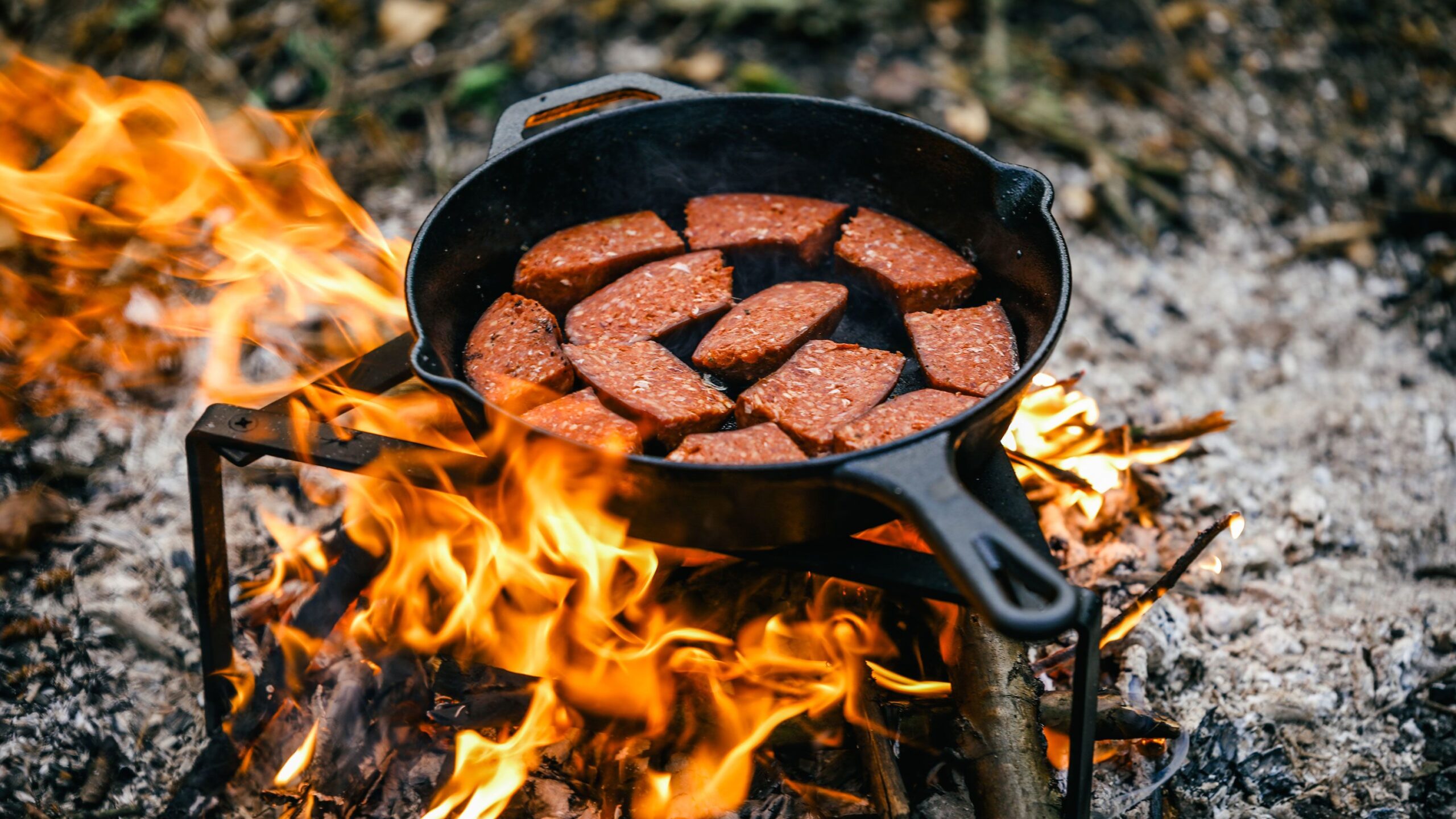 A cast iron skillet cooking sausages over a fire 