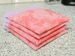 Stacked gallon ziplock bags filled with flattened ground beef, prepared for easy storage in a camping cooler