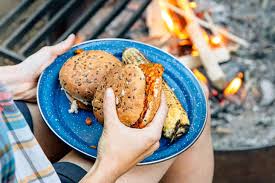 A person holding a plate of sloppy joes next to a camp fire